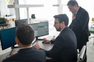 Colleagues in a modern office reviewing stock market trends and data on multiple screens.
